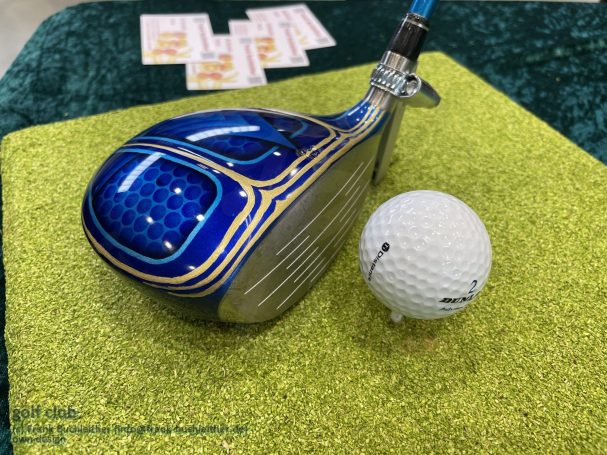 Blauer Golfschläger mit detailliertem Muster, daneben ein weißer Golfball.