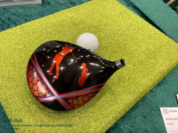Schwarze Golfschläger mit rotem Design, daneben ein Golfball.