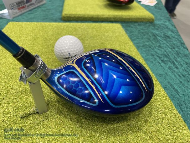 Blauer Golfschläger mit detailliertem Muster, daneben ein weißer Golfball.