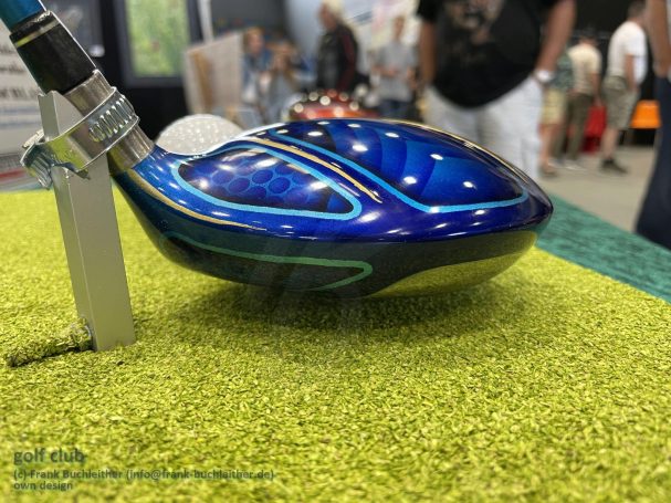 Blauer Golfschläger mit detailliertem Muster, daneben ein weißer Golfball.